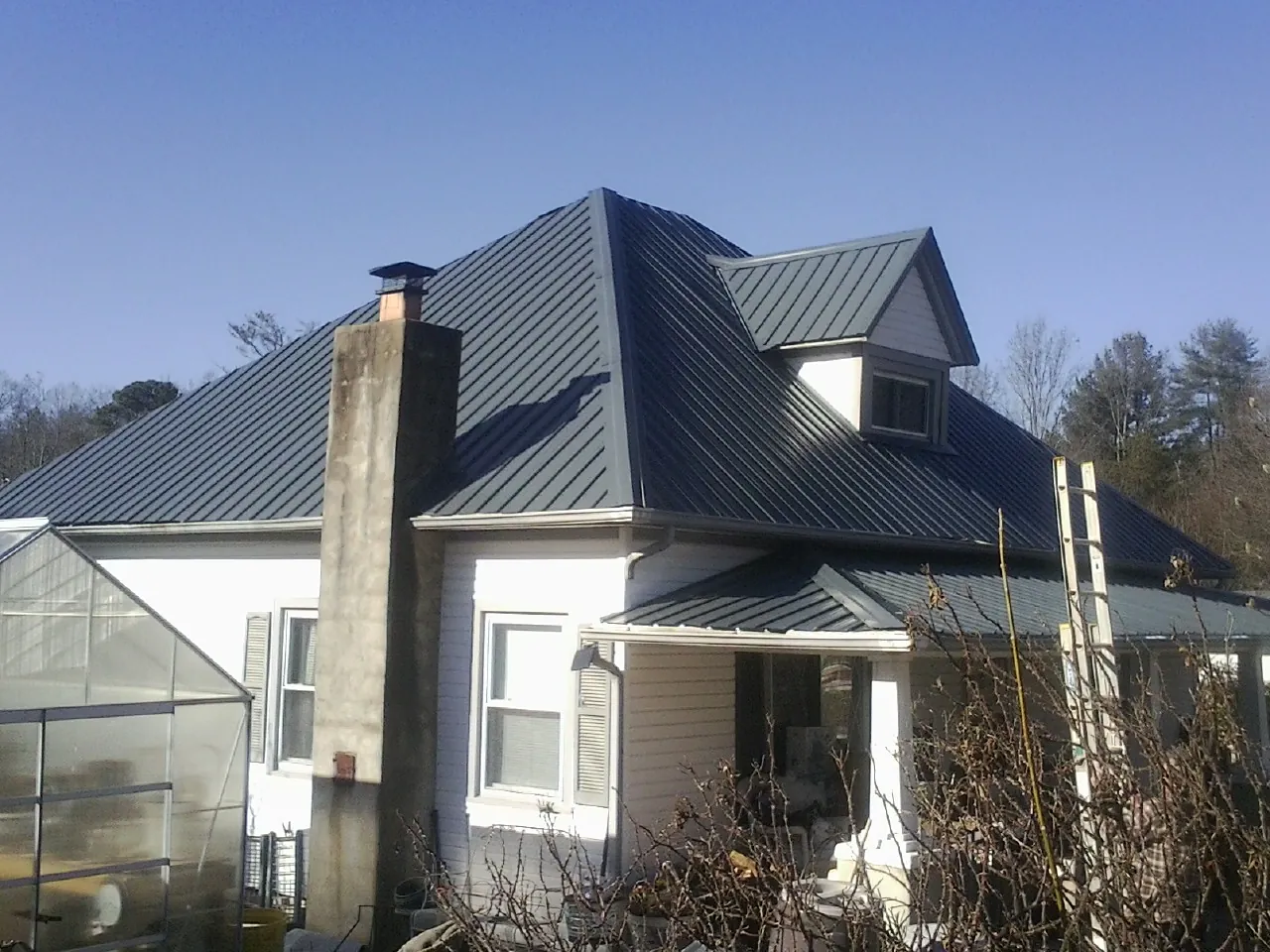 Dark blue standing seam metal roof on a white farmhouse with dormer — Slate & Tile Roof Repair by Roofing Brothers in Berlin Heights