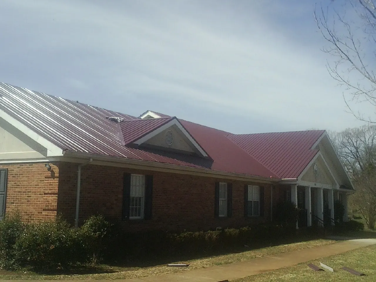 Red metal roof with gabled entries on a long brick building, from a Hail Damage Roof Repair job in Berlin Heights