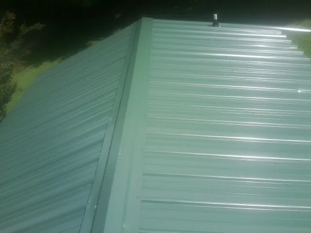 New green metal panels meeting at the ridge of a roof — Flat Roof Repair work by our crew in Berlin Heights