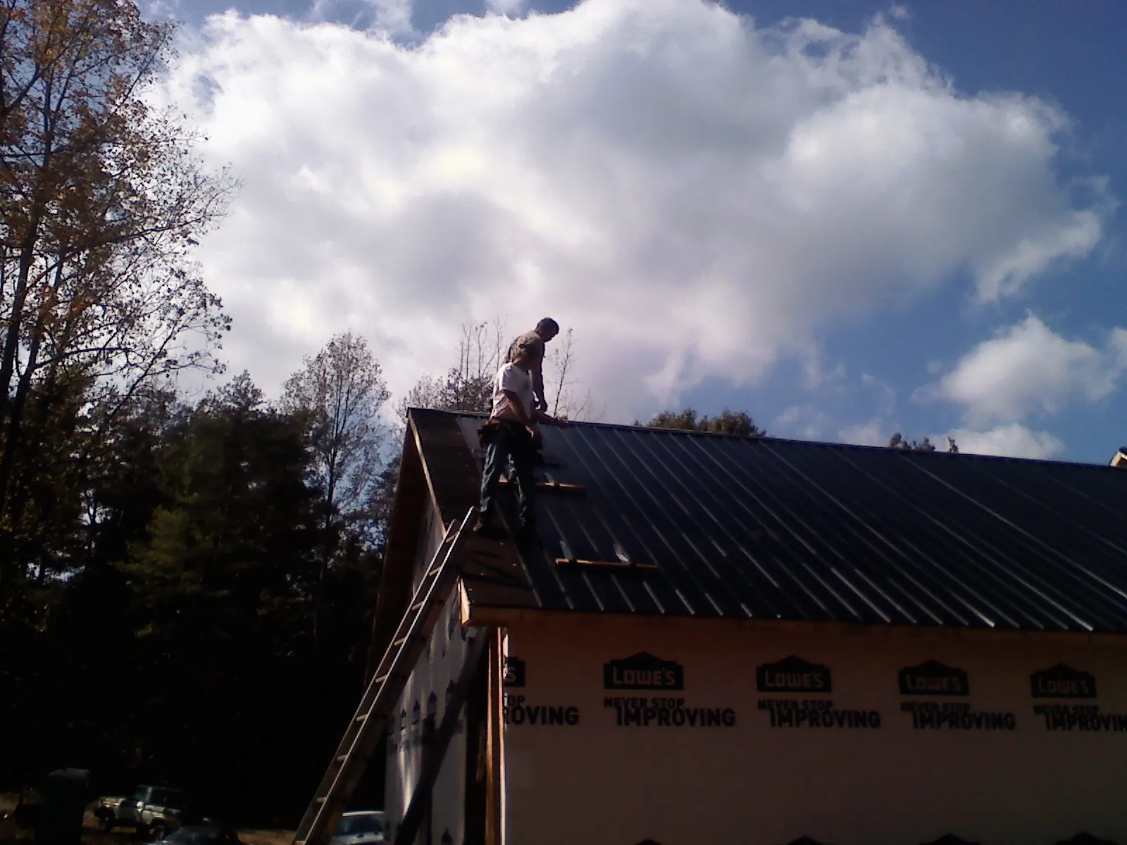 Roofer fastening dark metal panels high against a cloudy sky, from a Roof Inspection job in Berlin Heights