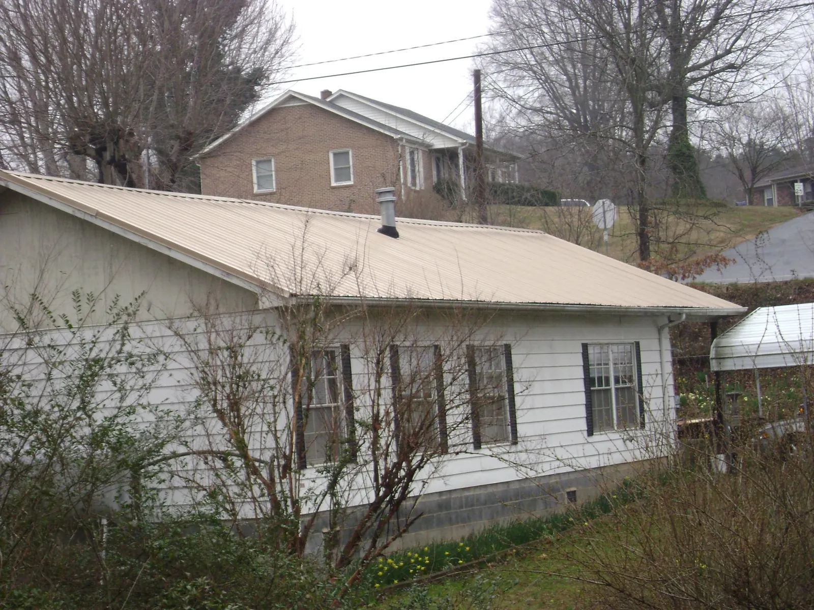 Tan metal roof on a white sided house set into a hillside — Commercial Roofing by Roofing Brothers in Berlin Heights