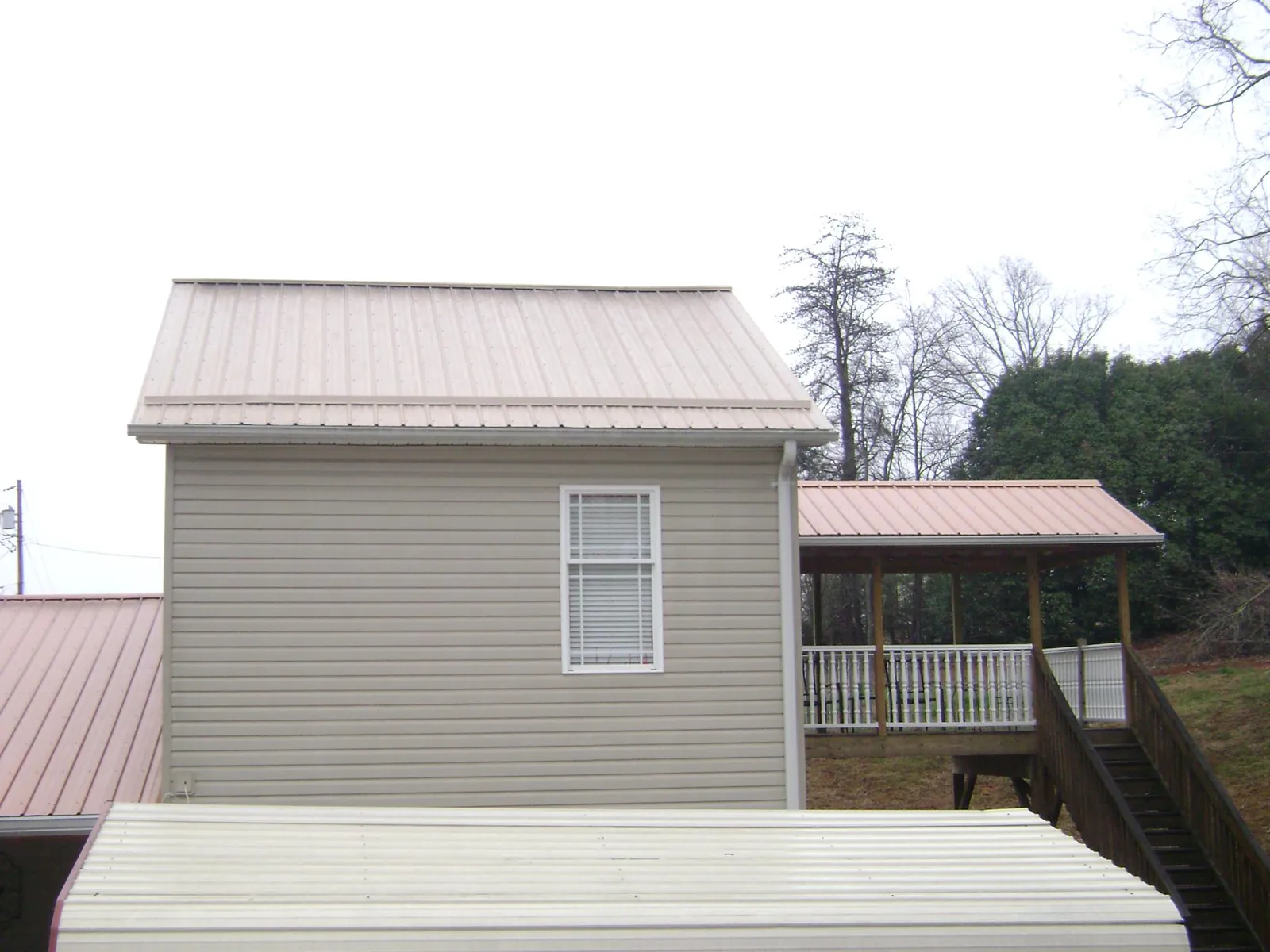 Tan metal roofs on a two story addition and attached porch, from a Roof Replacement job in Berlin Heights